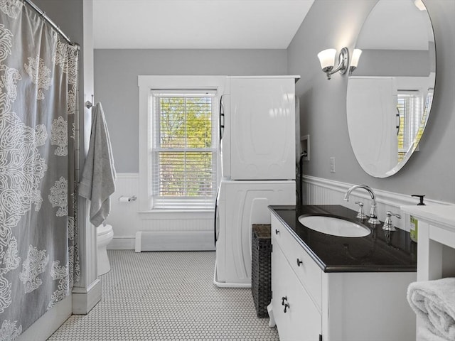 bathroom featuring vanity, toilet, tile patterned floors, a wainscoted wall, and stacked washer / drying machine