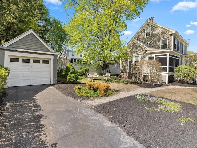 view of front of home featuring a detached garage, a sunroom, a chimney, an outdoor structure, and driveway