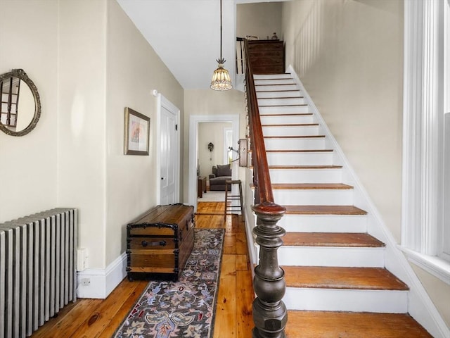 stairs with radiator heating unit, baseboards, and wood-type flooring