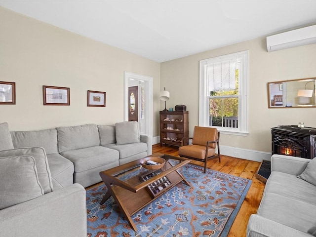 living room with an AC wall unit, a wood stove, baseboards, and wood finished floors