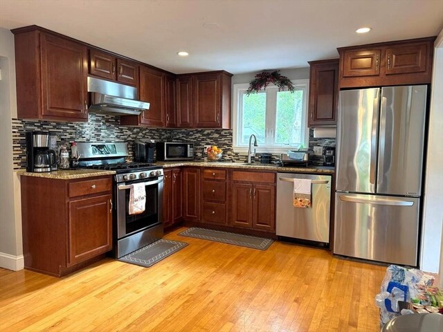 103 Sycamore St, Holbrook, MA 02343 - kitchen featuring appliances with stainless steel finishes, under cabinet range hood, light wood-style flooring, backsplash, and stone countertops