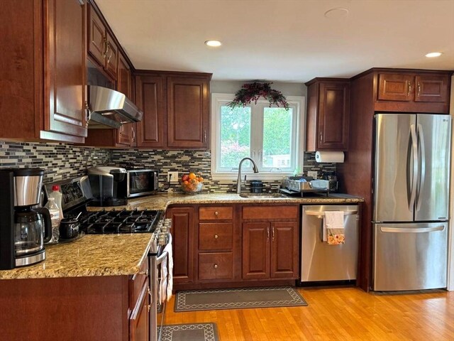 103 Sycamore St, Holbrook, MA 02343 - kitchen featuring appliances with stainless steel finishes, wall chimney range hood, light wood-type flooring, a sink, and backsplash