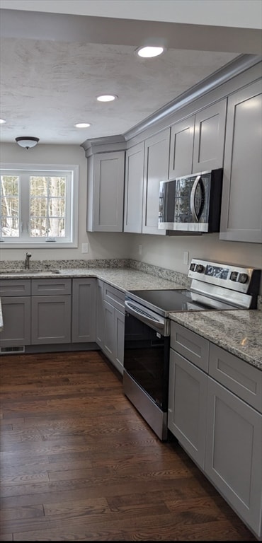 kitchen with appliances with stainless steel finishes, dark hardwood / wood-style floors, gray cabinets, light stone countertops, and sink