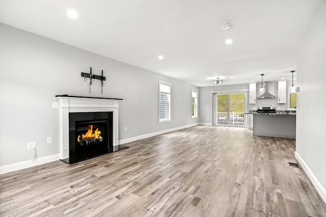 unfurnished living room with a lit fireplace, light wood finished floors, visible vents, and baseboards