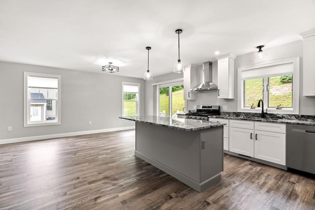 kitchen featuring a center island, appliances with stainless steel finishes, a sink, wall chimney range hood, and dark stone counters