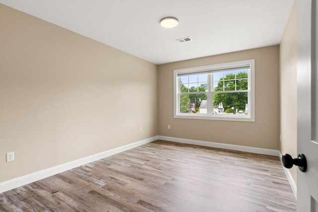 empty room featuring wood finished floors, visible vents, and baseboards