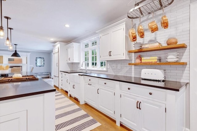 kitchen with light wood-style floors, ornamental molding, white cabinets, dark countertops, and decorative backsplash