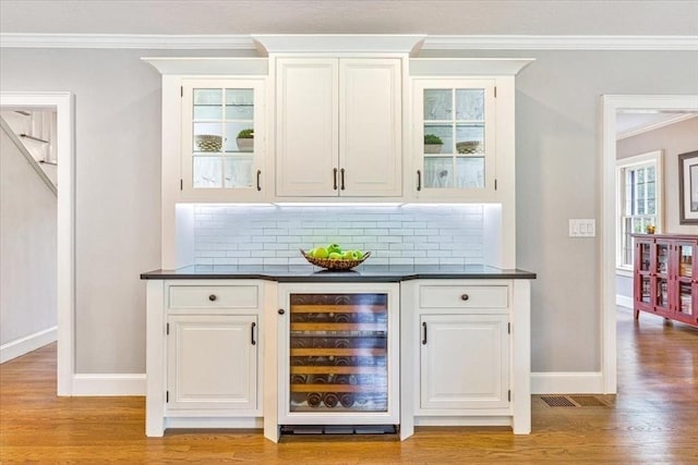 bar featuring ornamental molding, light wood finished floors, beverage cooler, and decorative backsplash