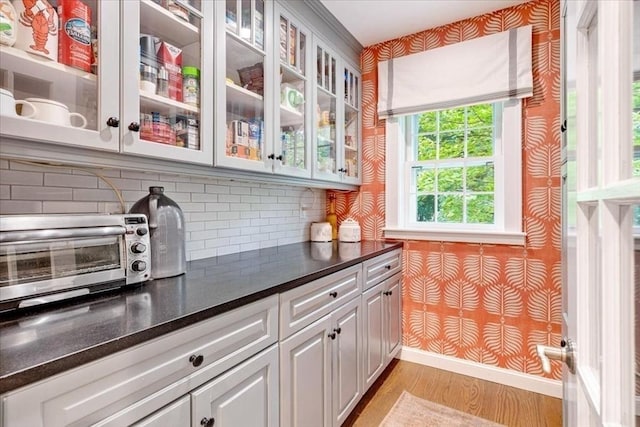 kitchen with glass insert cabinets, dark countertops, light wood-style floors, wallpapered walls, and a toaster