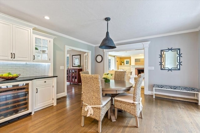 dining space featuring baseboards, ornamental molding, wine cooler, wood finished floors, and a lit fireplace