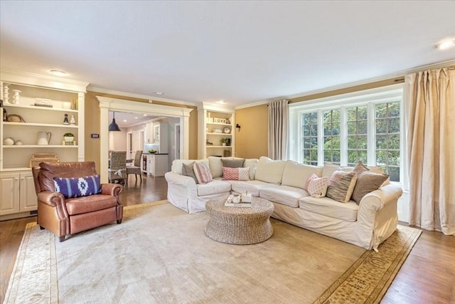 living room with wood finished floors, ornamental molding, and built in shelves