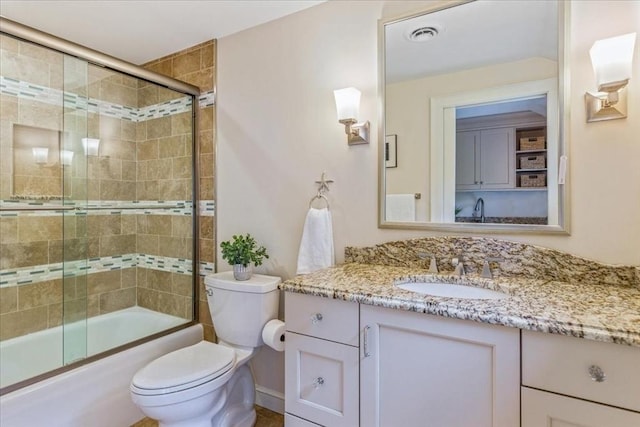 bathroom featuring toilet, vanity, combined bath / shower with glass door, and visible vents