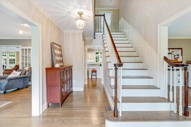 staircase with ornamental molding, baseboards, a notable chandelier, and wood finished floors