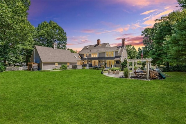 back of property at dusk with a chimney, a pergola, a patio area, and a yard