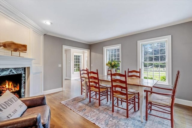 dining space with light wood-style flooring, crown molding, a premium fireplace, and a wealth of natural light