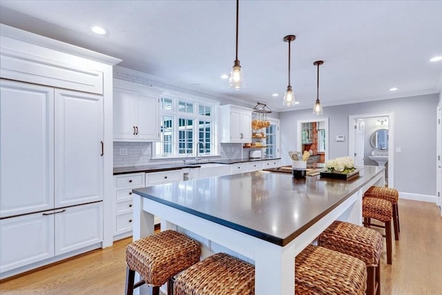 kitchen featuring a sink, dark countertops, a breakfast bar, light wood-style floors, and white cabinetry