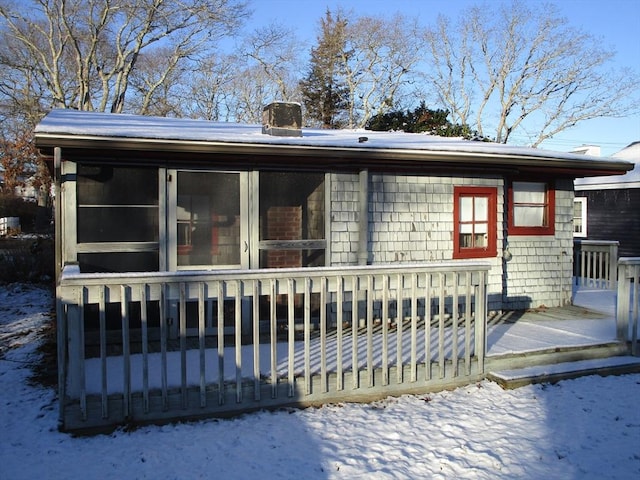 snow covered back of property with a deck and a sunroom