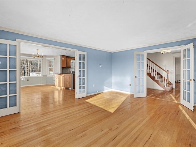 unfurnished living room featuring french doors, crown molding, a chandelier, and light hardwood / wood-style flooring