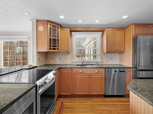 kitchen featuring light hardwood / wood-style floors, appliances with stainless steel finishes, tasteful backsplash, dark stone countertops, and sink