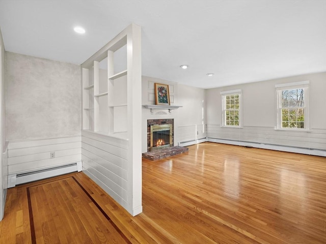 unfurnished living room featuring built in shelves, baseboard heating, a brick fireplace, and wood-type flooring