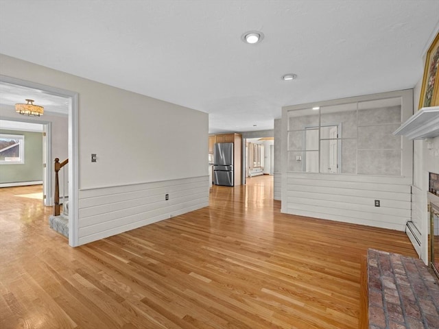 unfurnished living room with light hardwood / wood-style flooring, wooden walls, and a baseboard radiator