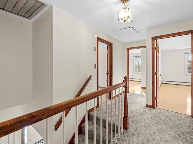 corridor with a baseboard heating unit and light carpet