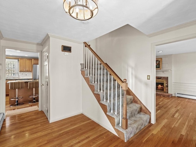 stairs featuring a brick fireplace, baseboard heating, hardwood / wood-style floors, and an inviting chandelier