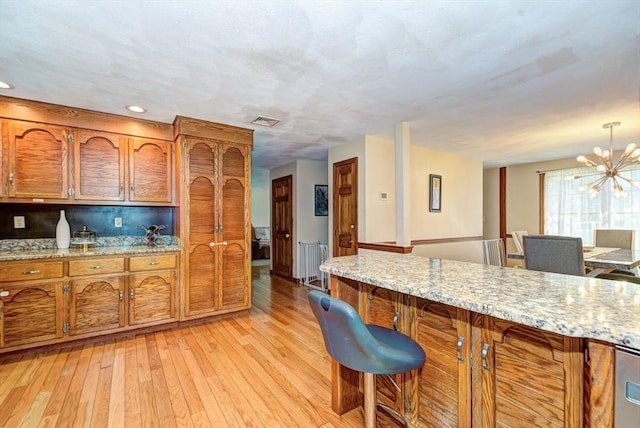 11 Balmoral Dr, Methuen, MA 01844 - kitchen with brown cabinetry, light wood-style floors, a breakfast bar, a chandelier, and light stone countertops