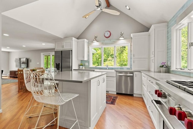 kitchen with appliances with stainless steel finishes, plenty of natural light, a sink, white cabinetry, and vaulted ceiling