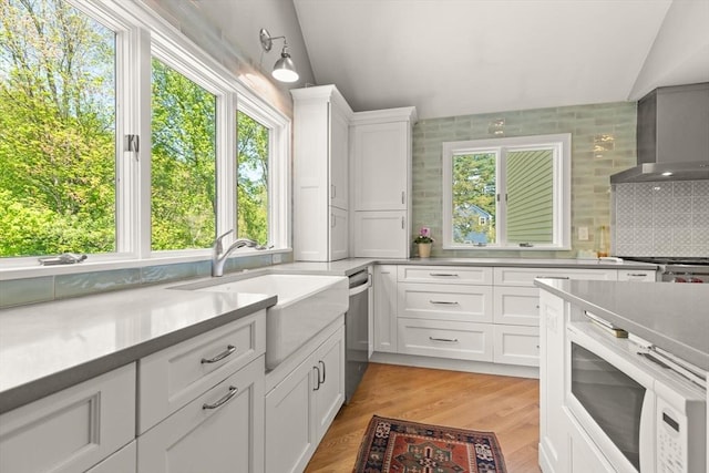 kitchen featuring white microwave, light countertops, white cabinetry, vaulted ceiling, and backsplash