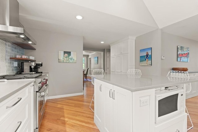kitchen with high end stainless steel range oven, white microwave, wall chimney range hood, light countertops, and white cabinetry