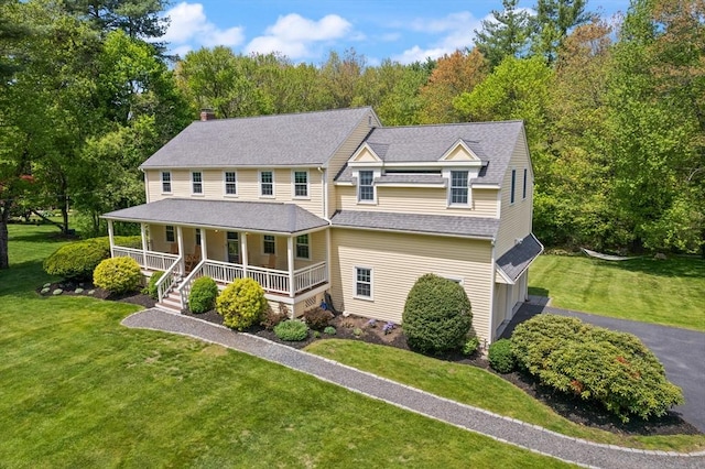 view of front of house featuring covered porch, a chimney, a front yard, asphalt driveway, and a shingled roof