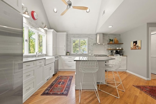 kitchen featuring wall chimney range hood, a sink, appliances with stainless steel finishes, ceiling fan, and a kitchen island