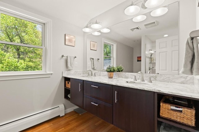 bathroom featuring a baseboard heating unit, wood finished floors, vaulted ceiling, double vanity, and healthy amount of natural light