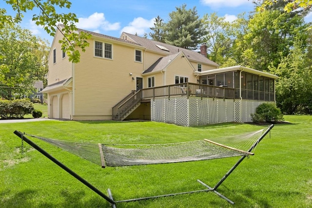 back of house featuring a sunroom, stairway, an attached garage, a wooden deck, and a yard