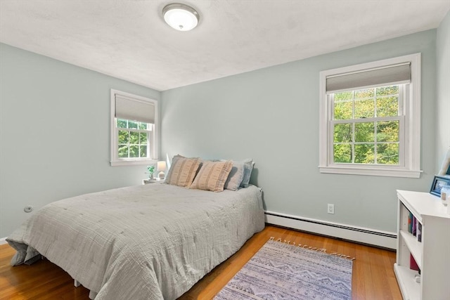 bedroom featuring a baseboard heating unit, multiple windows, and wood finished floors