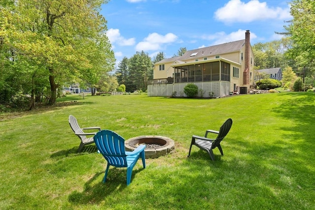 view of grassy yard featuring a fire pit, a sunroom, and cooling unit
