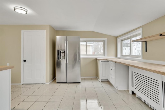 kitchen featuring light tile patterned floors, stainless steel fridge with ice dispenser, lofted ceiling, white cabinetry, and built in desk