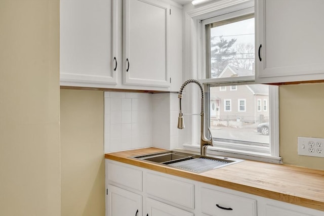 kitchen with white cabinets, butcher block counters, tasteful backsplash, and a sink