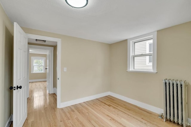 empty room with light wood finished floors, radiator heating unit, and baseboards