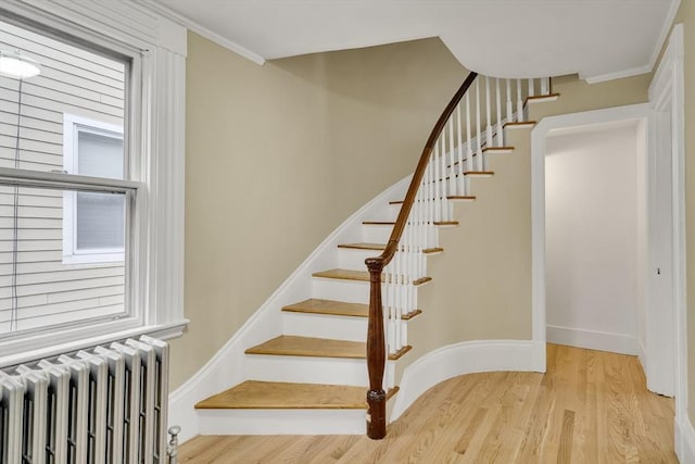 stairs with crown molding, radiator heating unit, wood finished floors, plenty of natural light, and baseboards