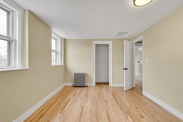 unfurnished bedroom with a closet, radiator, baseboards, and wood finished floors