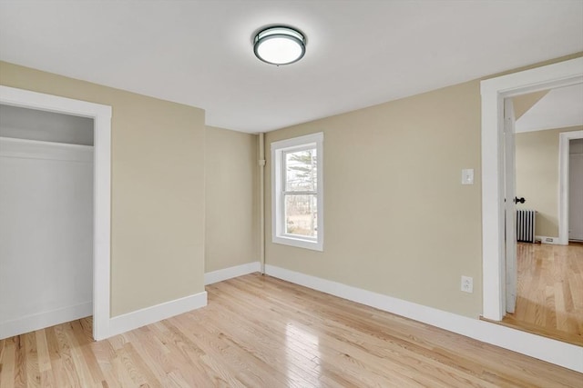 unfurnished bedroom featuring a closet, radiator heating unit, wood finished floors, and baseboards