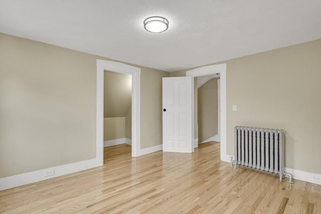 empty room with light wood-style floors, baseboards, and radiator heating unit