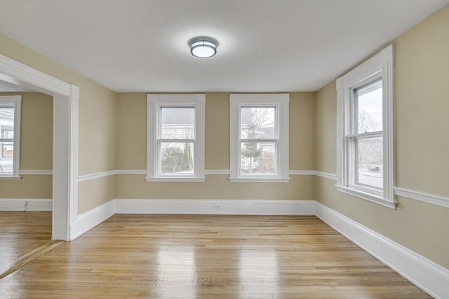 spare room with baseboards, light wood-type flooring, and a healthy amount of sunlight