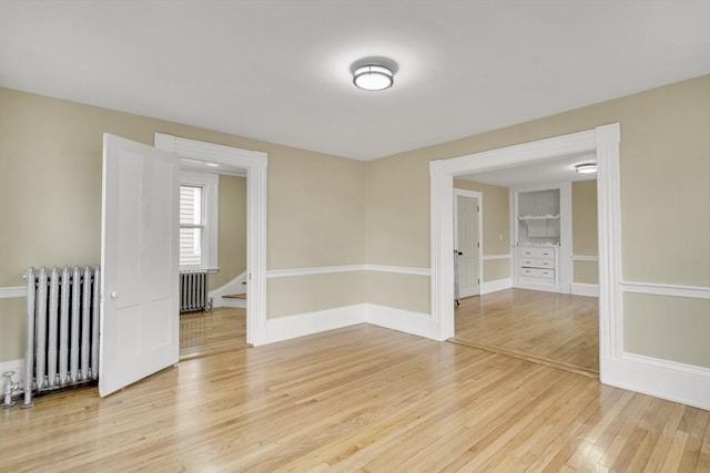 empty room with light wood-style floors, radiator, and baseboards