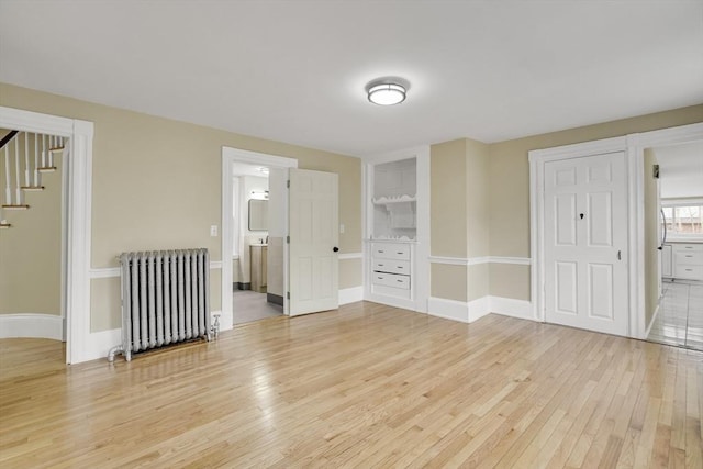 unfurnished room with stairs, radiator heating unit, light wood-style flooring, and baseboards