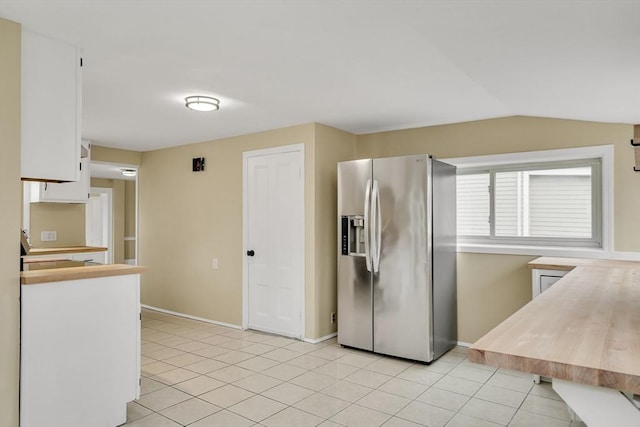 kitchen with light tile patterned floors, stainless steel fridge with ice dispenser, white cabinetry, vaulted ceiling, and baseboards