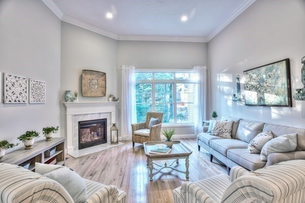 living room with light hardwood / wood-style floors, ornamental molding, and a high end fireplace