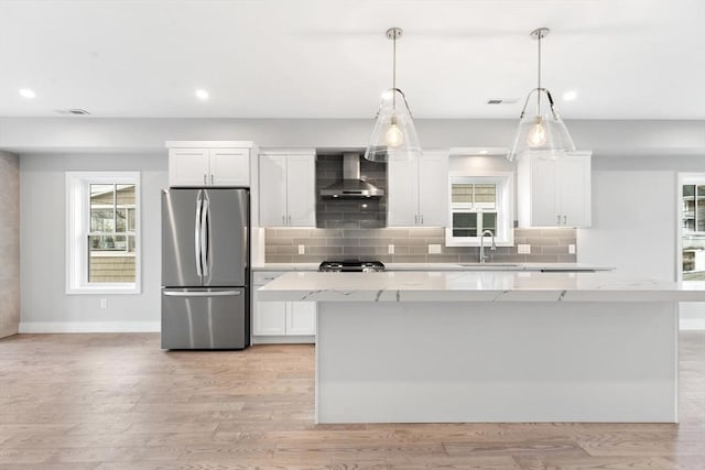 kitchen with light wood-type flooring, freestanding refrigerator, white cabinets, wall chimney exhaust hood, and tasteful backsplash